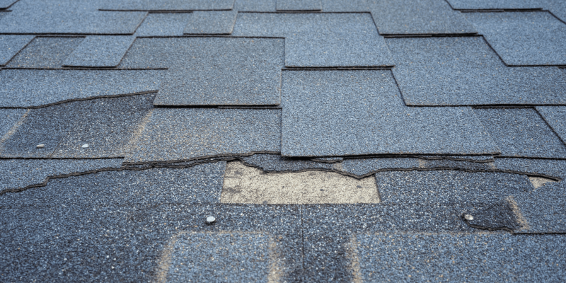 Damaged asphalt shingles on a roof with a missing piece